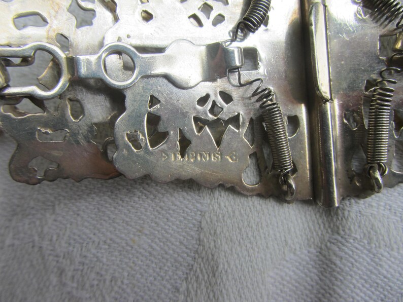 May include: Silver-toned metal clasp with intricate cut-out design and spring closures. The clasp is marked "Imprint's".