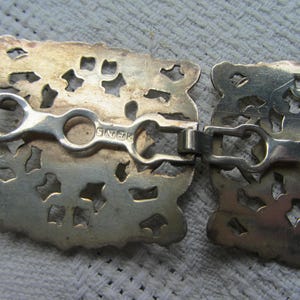 May include: A silver filigree belt buckle with a decorative design and the inscription "Sterling" on the back.