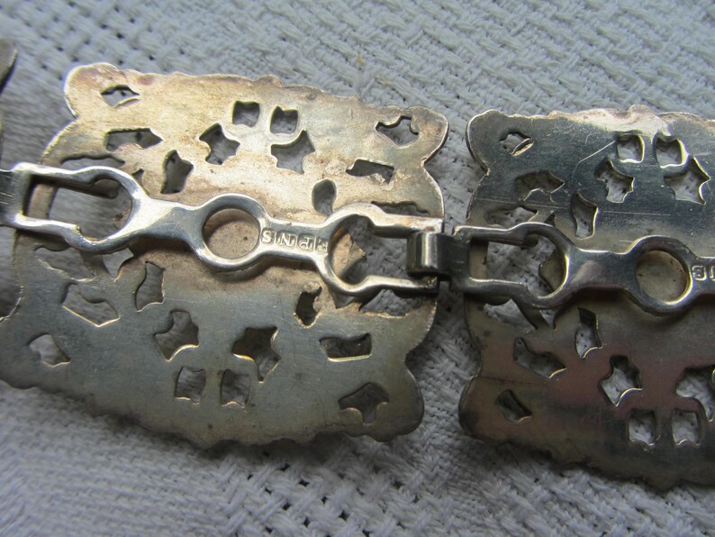 May include: A silver filigree belt buckle with a decorative design and the inscription "Sterling" on the back.