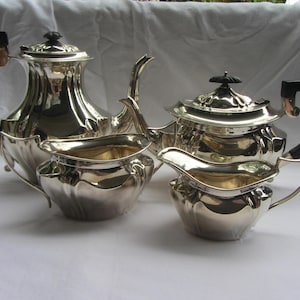 May include: A silver tea set comprising a teapot, creamer and sugar bowl. The teapot has a black handle and a silver lid. The creamer and sugar bowl have silver handles.