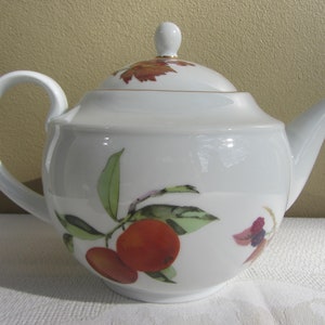 May include: White porcelain teapot with a lid and a floral design featuring oranges and leaves. The teapot has a gold trim around the lid and spout.