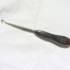 May include: A black and silver shoe horn with a curved handle and a hook at the end. The handle has a gold monogram.