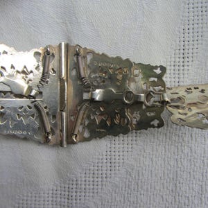 May include: Silver filigree belt buckle with a spring-loaded clasp. The buckle is marked "C. KINGSLEY & CO. BIRMINGHAM" and "ARTIAN".