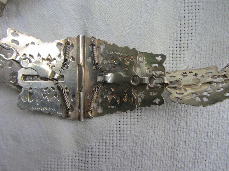 May include: Silver filigree belt buckle with a spring-loaded clasp. The buckle is marked "C. KINGSLEY & CO. BIRMINGHAM" and "ARTIAN".