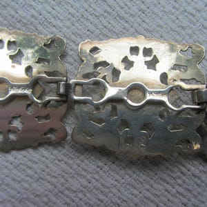 May include: Close-up of a silver filigree belt buckle with a decorative design. The buckle has a hinged clasp and is marked "Sterling".