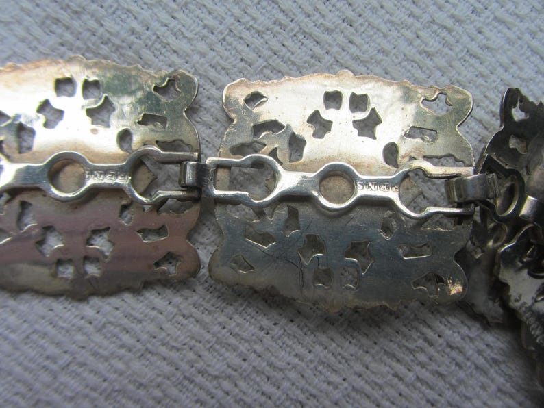 May include: Close-up of a silver filigree belt buckle with a decorative design. The buckle has a hinged clasp and is marked "Sterling".