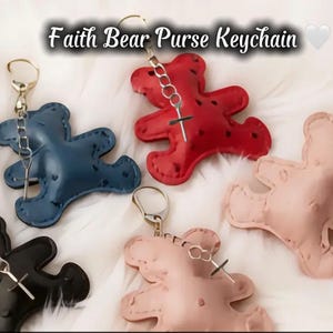 May include: A collection of leather bear-shaped purse keychains in various colors: black, blue, red, and pink. Each keychain has a silver-tone metal clasp and a cross charm. The text "Faith Bear Purse Keychain" is at the top.