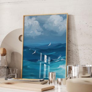 Puede incluir: Una pintura enmarcada de un paisaje mar&iacute;timo con nubes blancas y agua azul. La pintura presenta dos p&aacute;jaros blancos volando sobre el agua.