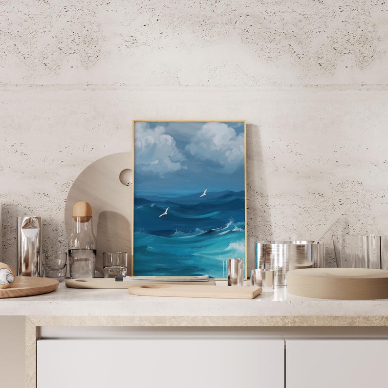 Puede incluir: Una pintura enmarcada de un paisaje mar&iacute;timo con agua azul y nubes blancas. Dos p&aacute;jaros blancos vuelan sobre el agua.