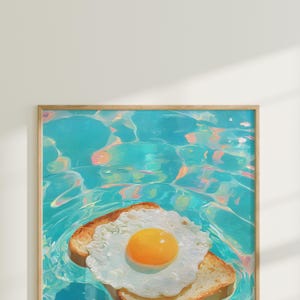 May include: A framed art print featuring a sunny-side-up egg on two slices of toast floating in a pool of turquoise water. The artwork has a whimsical, surreal quality, with vibrant colors and a playful theme.