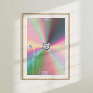 May include: A framed print of a colorful, abstract design with a silver circle in the center. The design resembles a CD or DVD with a rainbow effect.
