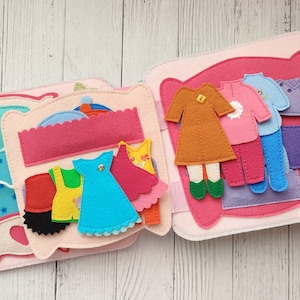 May include: A felt book with a variety of clothing items, including a dress, a skirt, a sweater, and pants. The book is designed for children to play with and learn about different types of clothing.