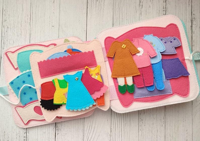May include: A felt book with a variety of clothing items, including a dress, a skirt, a sweater, and pants. The book is designed for children to play with and learn about different types of clothing.