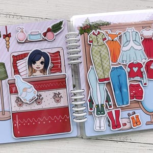 Pu&ograve; includere: Un libro di vestire magnetico a tema natalizio con una ragazza a letto da un lato e una variet&agrave; di opzioni di abbigliamento dall'altro. Le opzioni di abbigliamento includono pigiami, un maglione, jeans e stivali.