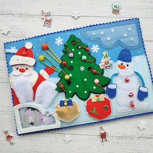 Peut inclure: Un tapis de jeu en feutre sur le thème de Noël avec un sapin de Noël vert, un bonhomme de neige, le Père Noël et une boîte cadeau. Le tapis est bleu avec des flocons de neige blancs et un nuage blanc.