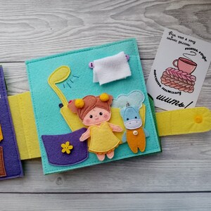 May include: A felt book for children with a purple, yellow, and blue cover. The book has a variety of felt characters and objects, including a girl, a unicorn, a shower, and a cup of coffee. The text on the book says "What I want to do now: sew!"