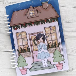Pu&ograve; includere: Una casa bianca con un tetto marrone e un cielo blu con stelle. La casa ha una porta rosa e due finestre con luci gialle. Ci sono due alberi di Natale verdi in vaso davanti alla casa. Una ragazza con lunghi capelli neri &egrave; in piedi sui gradini davanti alla casa. Indossa un vestito blu con un bordo di pelliccia bianca e calze bianche.
