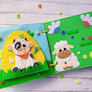 Pode incluir: Um livro de feltro para crian&ccedil;as com uma vaca e uma ovelha na capa. O livro &eacute; feito de feltro macio e colorido e tem uma variedade de texturas para as crian&ccedil;as explorarem.