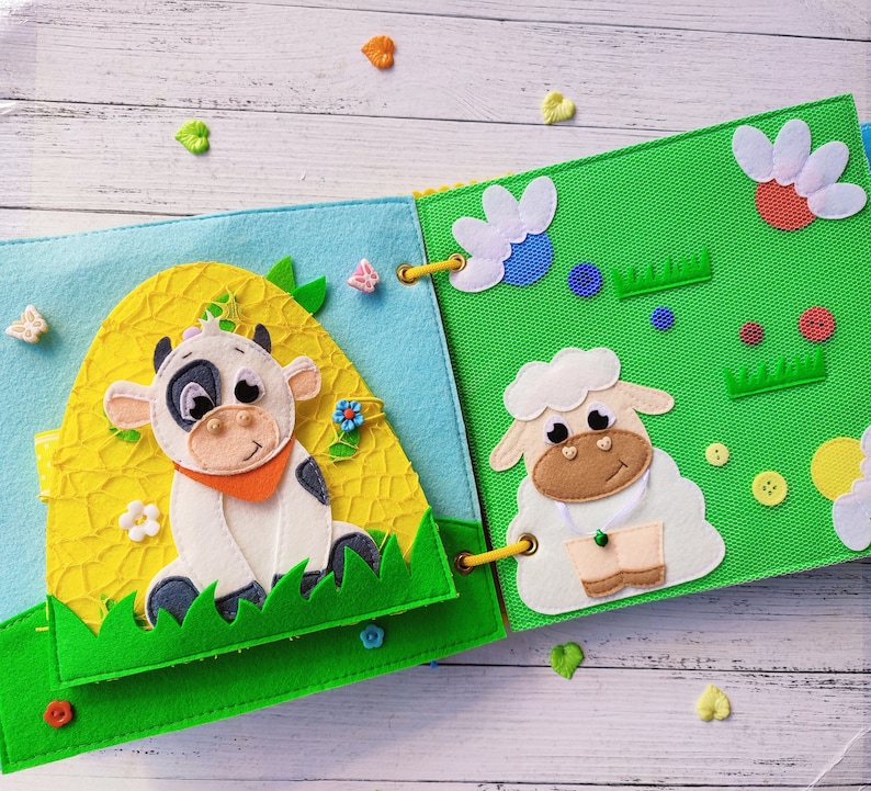Pode incluir: Um livro de feltro para crian&ccedil;as com uma vaca e uma ovelha na capa. O livro &eacute; feito de feltro macio e colorido e tem uma variedade de texturas para as crian&ccedil;as explorarem.