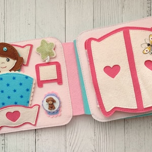May include: A pink felt book with a girl in a blue and white bed, a star, a nightstand, a dog, and a wardrobe with a butterfly on the front.