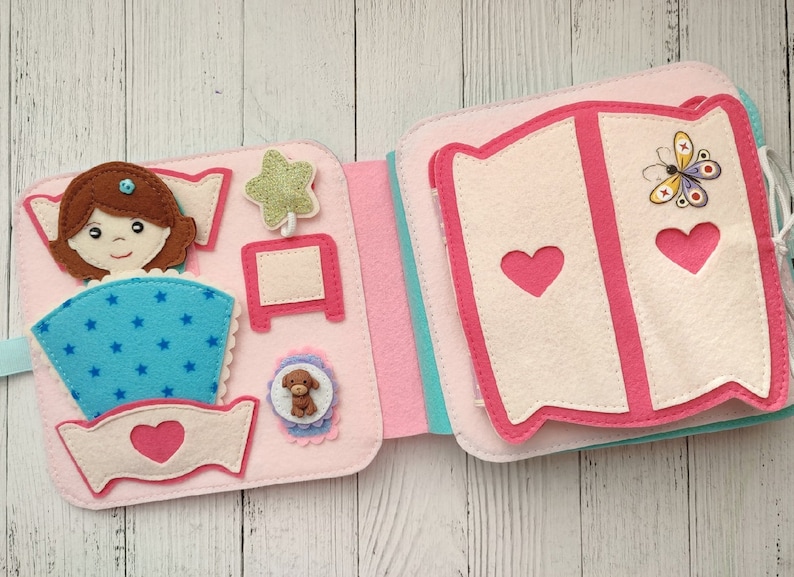 May include: A pink felt book with a girl in a blue and white bed, a star, a nightstand, a dog, and a wardrobe with a butterfly on the front.