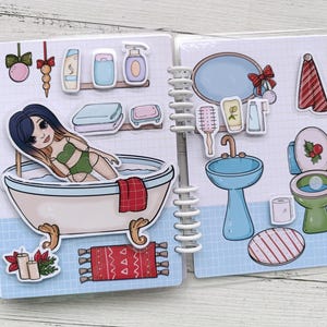 Pu&ograve; includere: Un libro di adesivi illustrato colorato con una ragazza in una vasca da bagno, un lavandino, un water e altri accessori per il bagno. Il libro ha una rilegatura a spirale.