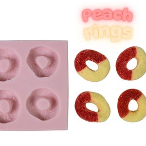Puede incluir: Un molde de silicona rosa con cuatro impresiones de anillos de melocotón, junto a cuatro caramelos de anillos de melocotón. Los caramelos son amarillos y rojos, con una capa de azúcar. El texto "Peach rings" se muestra.