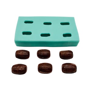 May include: A light teal silicone mold with six barrel-shaped cavities, alongside six dark brown barrel-shaped candies. The candies have a textured surface, and the mold is rectangular. The image is on a white background.
