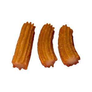 Può includere: Tre churros dorati con una consistenza a coste, presentati su sfondo bianco. I pasticcini fritti hanno un interno di colore chiaro visibile alle estremità, suggerendo un esterno croccante e un interno morbido. Un dessert classico.