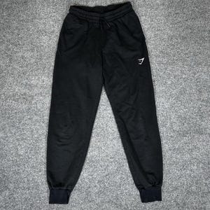 May include: Black sweatpants with a drawstring waist and elastic cuffs. A white logo is visible on the left leg. The pants have two side pockets and are made of a soft material.