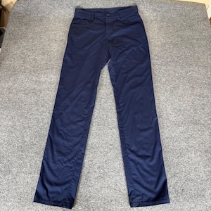 May include: Navy blue pants with a button closure and pockets. The pants are made of a smooth fabric and have a classic, straight-leg design. The pants are laid flat on a gray surface.