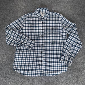 May include: A long-sleeve button-down shirt featuring a navy blue and white plaid pattern. The shirt includes a standard collar, a front button placket, and two chest pockets with button closures. The Gap brand label is visible at the inner neck.