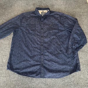 May include: A long-sleeved button-down shirt in navy blue, covered in a small, repeating floral pattern. The shirt features a classic collar and a small logo near the chest pocket. The brand name "BUFFALO DAVID BITTON" is visible on the collar.