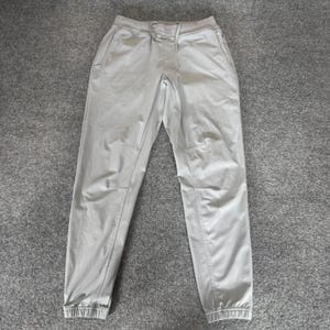 May include: Light gray joggers featuring an elastic waistband with a matching drawstring, side pockets, and ribbed cuffs at the ankles. The pants have a tapered leg design with visible seam detailing along the knees and thighs, providing a structured fit.