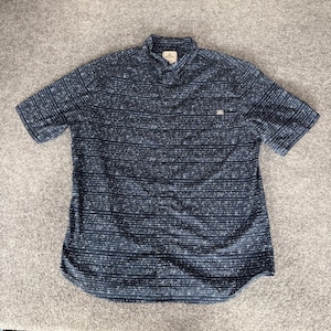 May include: A short-sleeve button-down shirt in dark navy blue featuring a repeating pattern of small white horizontal dashes and triangles. The shirt includes a standard collar, a front button placket, and a single chest pocket on the left side.