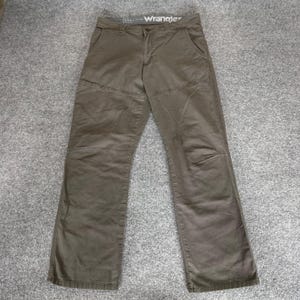 May include: Brown Wrangler pants with a straight leg design. The pants have a button and zipper closure, front pockets, and a small pocket on the right side. The brand name "Wrangler" is visible on the waistband.