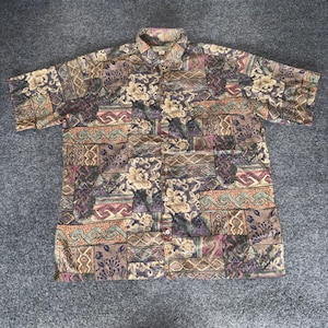 May include: Short-sleeved button-down shirt with a patchwork design. The shirt features a mix of floral and geometric patterns in shades of brown, beige, purple, and teal. The shirt has a collared neckline and a button-up front.