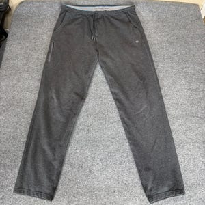 May include: Dark gray sweatpants with a drawstring waist and a small logo on the right leg. The pants have a straight leg design and a small pocket on the left side. The waistband has a light blue trim.