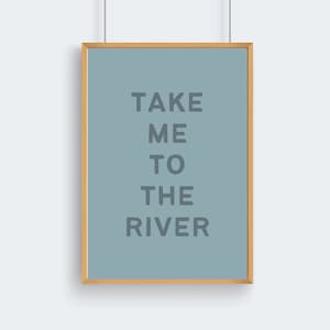 May include: A framed art print with the text "TAKE ME TO THE RIVER" in gray letters on a light blue background. The frame is a light brown color, and the print is hanging against a white wall.