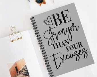 May include: Gray spiral notebook with the text "BE STRONGER THAN YOUR EXCUSES" in black lettering. A small heart symbol is above the word "BE".