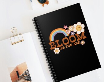 May include: Black spiral notebook with a rainbow and flowers design. The text "Bloom as you are" is printed in orange on the cover.