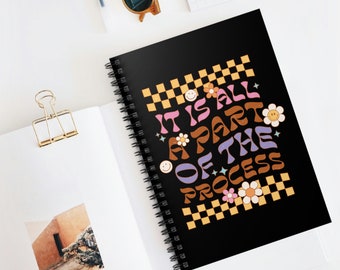 May include: Black spiral notebook with a colorful graphic that says "It is all a part of the process" with a checkered background and smiley faces.