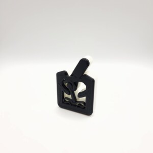 May include: A 3D-printed, black and white object with a rectangular base and a stylized design. The black element features a cutout design, and the white section is a solid block. The object has a modern, geometric aesthetic.