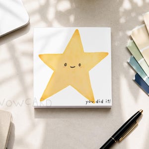 May include: A square white sticky note featuring a yellow watercolor-style star illustration with a simple smiling face. The text "you did it!" is printed in small black letters in the bottom right corner of the note, which has a smooth finish.