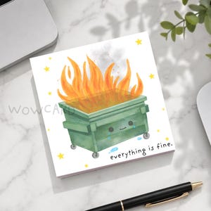 May include: A square greeting card featuring a watercolor illustration of a green dumpster on wheels filled with orange and yellow flames. The dumpster has a smiling face and blue teardrops. Yellow stars surround it with the text everything is fine.