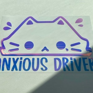 May include: A holographic sticker with a purple outline of a cat face and the text "ANXIOUS DRIVER" in blue.