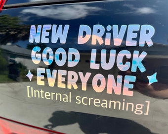 May include: A black car with a sticker that reads "NEW DRIVER GOOD LUCK EVERYONE [Internal screaming]" in rainbow holographic letters.