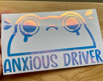 Puede incluir: Una pegatina blanca con un contorno azul de una rana de dibujos animados con una cara triste y ojos en forma de lágrima. La rana está llorando y el texto "ANXIOUS DRIVER" está escrito debajo de la rana en letras azules.