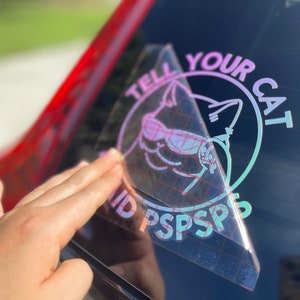 K&ouml;nnte beinhalten: Ein holografischer Aufkleber mit einem rosa und violetten Farbverlauf. Der Aufkleber zeigt eine Katze mit Sonnenbrille und den Text "Tell Your Cat" und "ID PSPSPS".