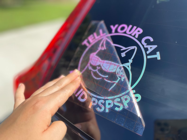 K&ouml;nnte beinhalten: Ein holografischer Aufkleber mit einem rosa und violetten Farbverlauf. Der Aufkleber zeigt eine Katze mit Sonnenbrille und den Text "Tell Your Cat" und "ID PSPSPS".